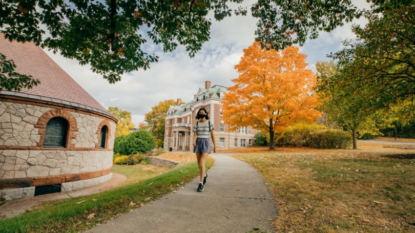 A student walks through campus in the fall foliage.