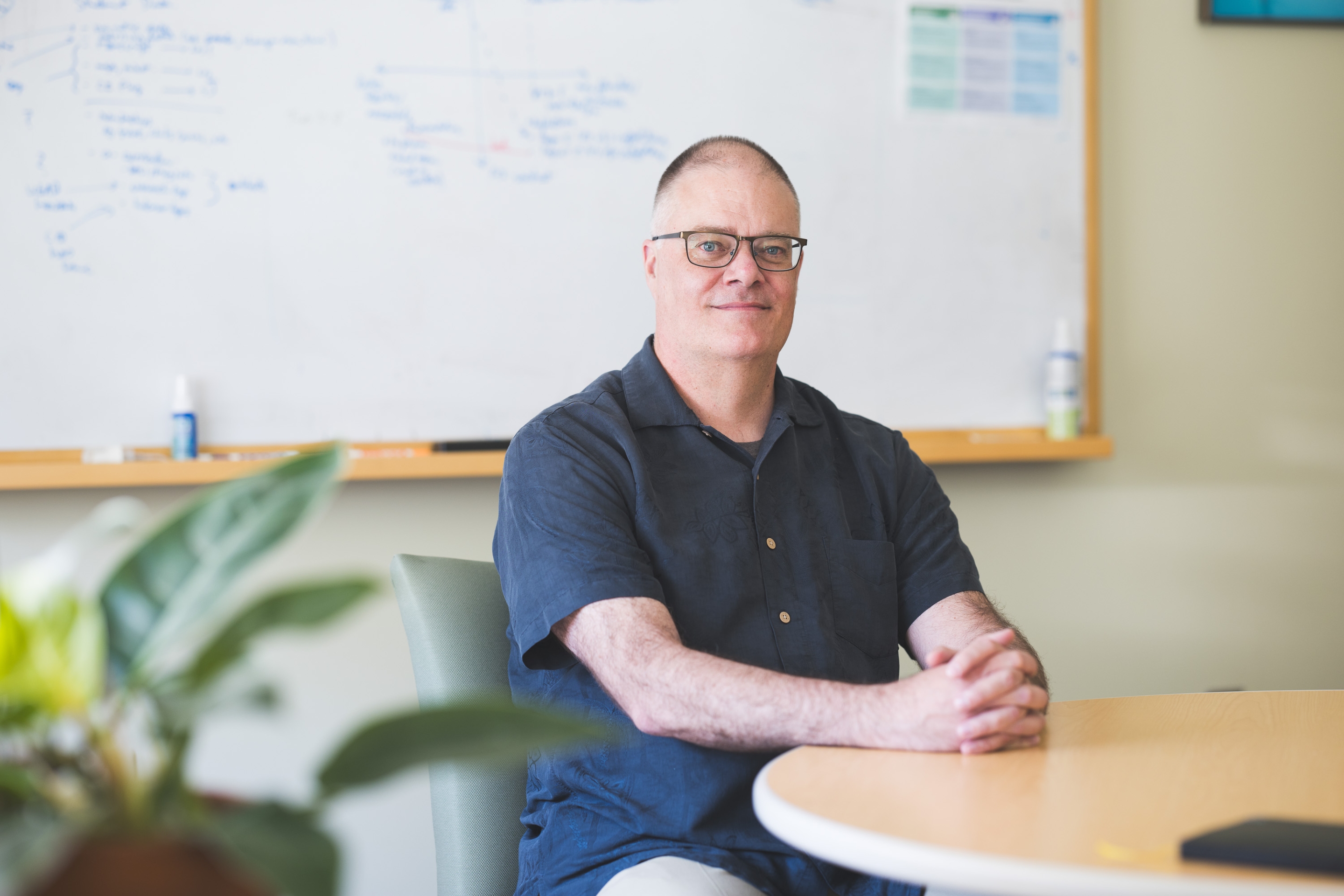 A photograph of Scott Pauls sitting at a table in front of a whiteboard.  Image Credit: Katherine Lenhart, 2025 