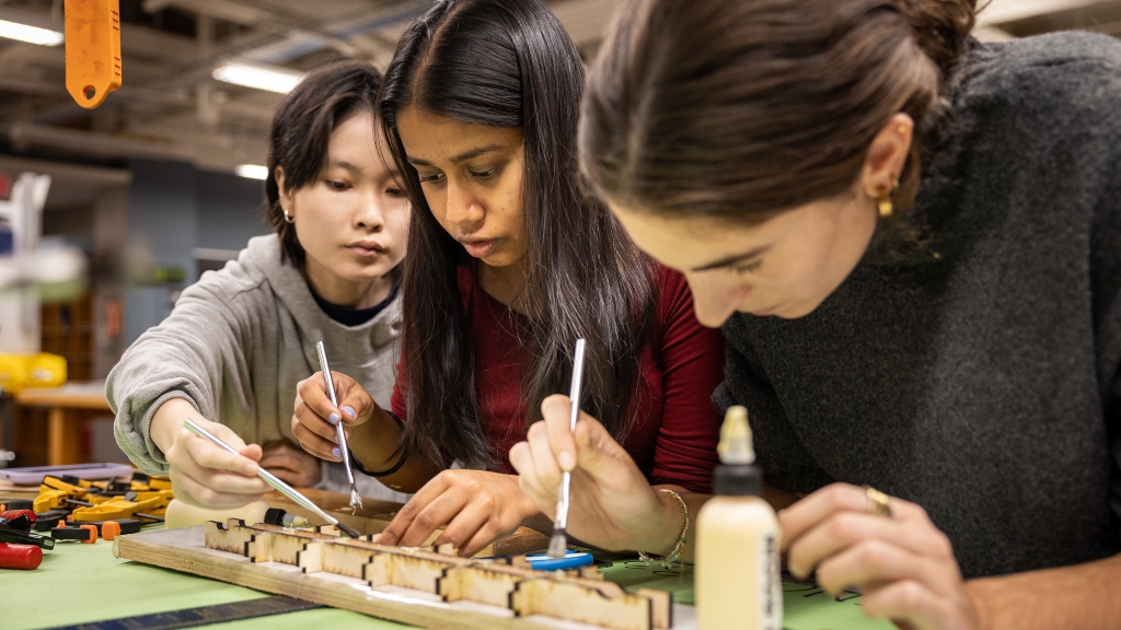 Three students working on a model sitting on a table top. 