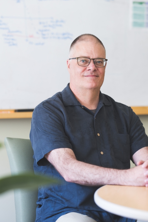 A photograph of Scott Pauls sitting at a table in front of a whiteboard. Image Credit: Katherine Lenhart, 2025